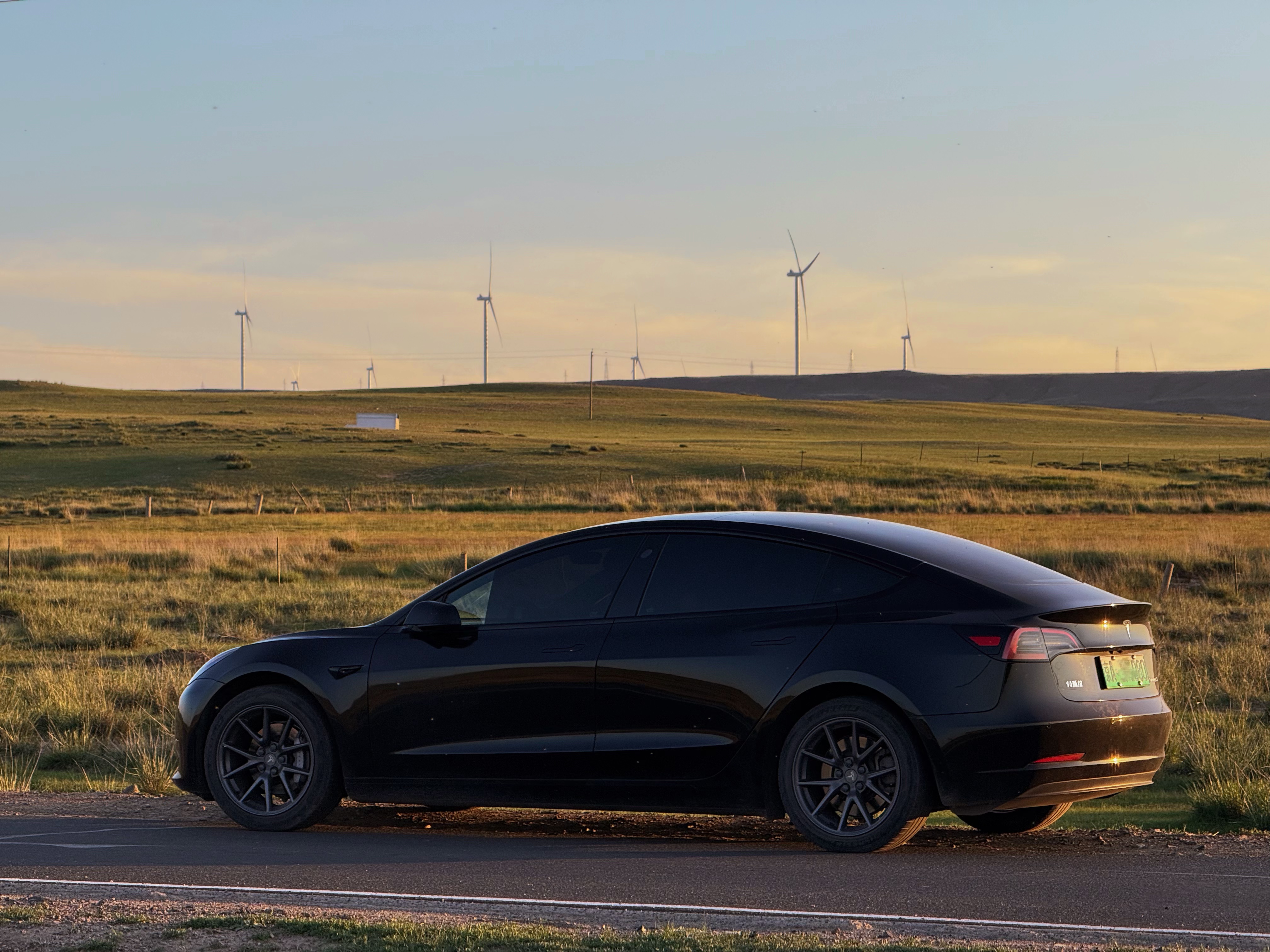 Tesla parked in front of wind turbines at sunset